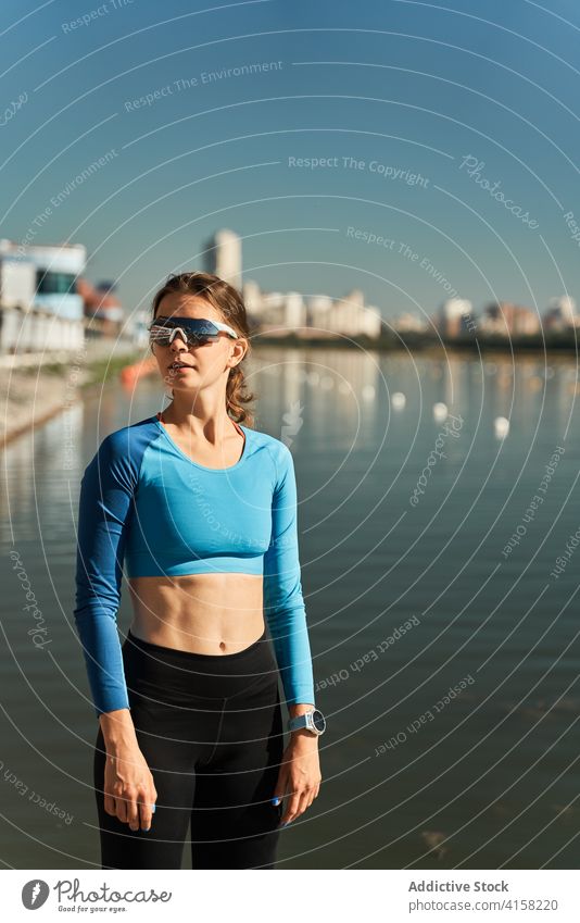 Schlanke aktive Frau in Sportkleidung und Sonnenbrille steht in der Nähe von Fluss sportlich selbstbewusst passen schlank Training Fitness Tracker