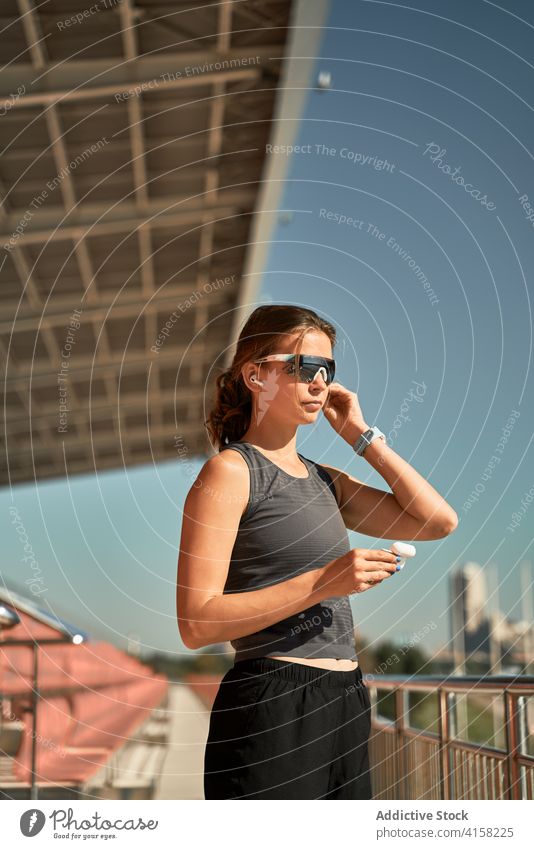Sportliche Frau, die sich im Stadion Ohrstöpsel aufsetzt sportlich Sonnenbrille passen aktiv trendy Stil angezogen ausrichten Drahtlos Kopfhörer tws