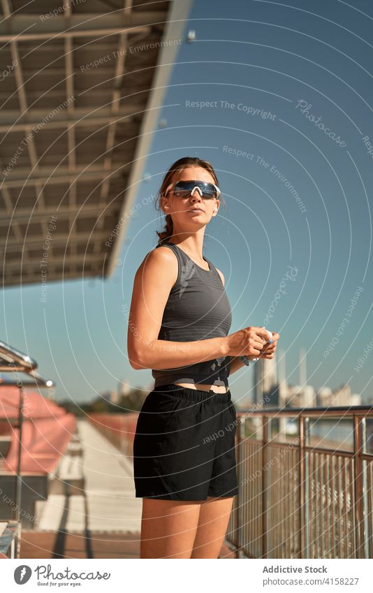 Sportliche Frau, die sich im Stadion Ohrstöpsel aufsetzt sportlich Sonnenbrille passen aktiv trendy Stil angezogen ausrichten Drahtlos Kopfhörer tws