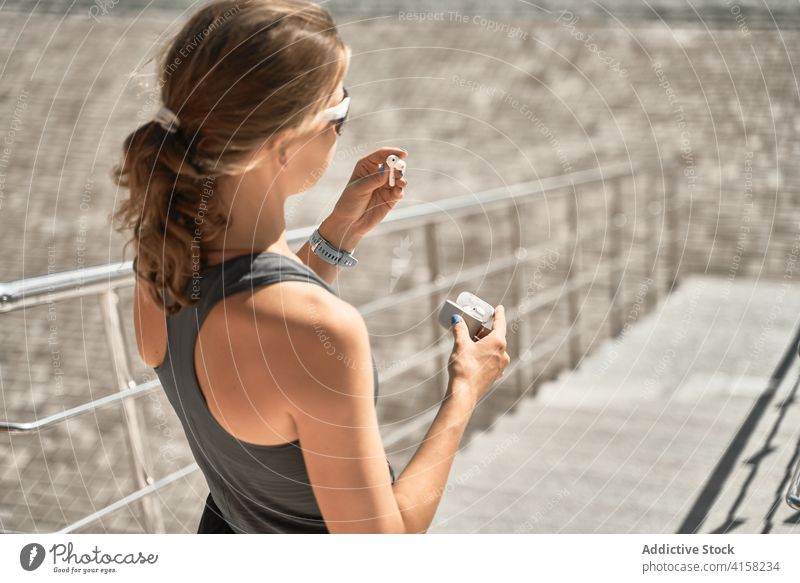Sportliche Frau, die sich im Treppenhaus Ohrstöpsel aufsetzt sportlich Sonnenbrille passen aktiv trendy Stil angezogen ausrichten Drahtlos Kopfhörer tws