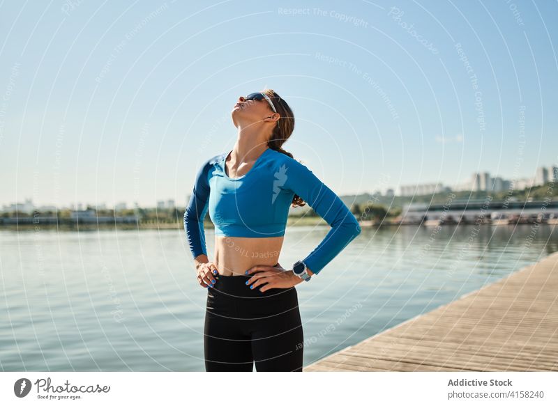 Schlanke aktive Frau in Sportkleidung und Sonnenbrille steht in der Nähe von Fluss sportlich selbstbewusst passen schlank Training Fitness Tracker