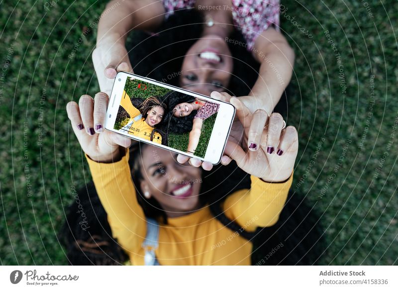 Erfreute afroamerikanische Frauen machen ein Selfie auf dem Rasen Freundschaft bester Freund Smartphone Gras Lügen Zusammensein charmant ethnisch schwarz