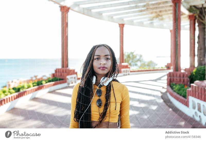 Schwarze Frau mit Kopfhörern an der Uferböschung Geflecht Vorschein charmant Spazierweg Individualität Sommer kreativ Windstille ethnisch schwarz Afroamerikaner