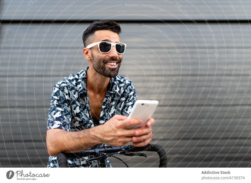 Fröhlicher Mann mit Smartphone auf der Straße soziale Netzwerke Großstadt benutzend Fahrrad fettarm trendy Stil männlich maskulin gutaussehend Telefon Mobile