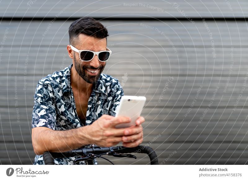 Fröhlicher Mann mit Smartphone auf der Straße soziale Netzwerke Großstadt benutzend Fahrrad fettarm trendy Stil männlich maskulin gutaussehend Telefon Mobile