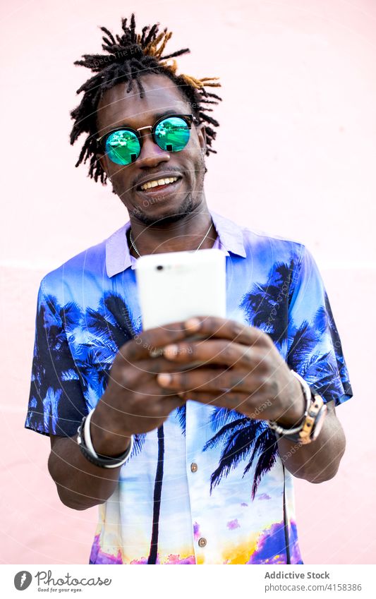 Stylischer schwarzer Mann benutzt Smartphone in der Stadt tropisch Hemd Stil Outfit trendy Vorschein benutzend soziale Netzwerke männlich ethnisch