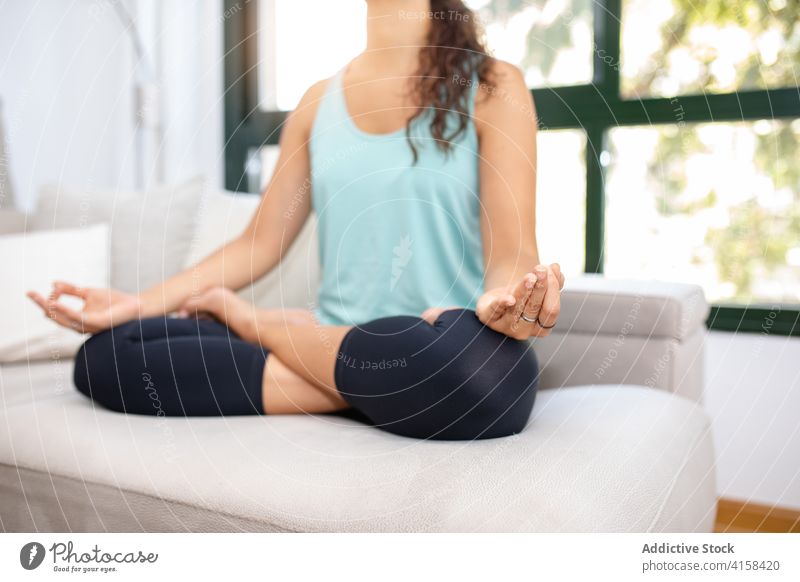 Friedliche Frau meditiert in Lotus-Pose zu Hause Achtsamkeit Stressabbau Yoga padmasana meditieren sich[Akk] entspannen Vitalität ruhig üben Sofa Mudra