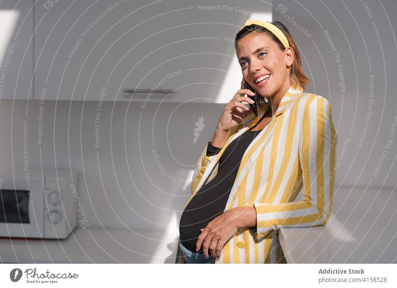 Stilvolle schwangere Frau spricht am Telefon in der Küche heimwärts Smartphone reden Anruf trendy modern jung Streifen gelb Gerät Apparatur Lifestyle sprechen