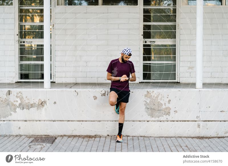 Sportler, der auf einer Straße in der Stadt die Zeit auf seiner Armbanduhr überprüft Läufer Bestimmen Sie Großstadt Mann Sportbekleidung Sommer passen männlich