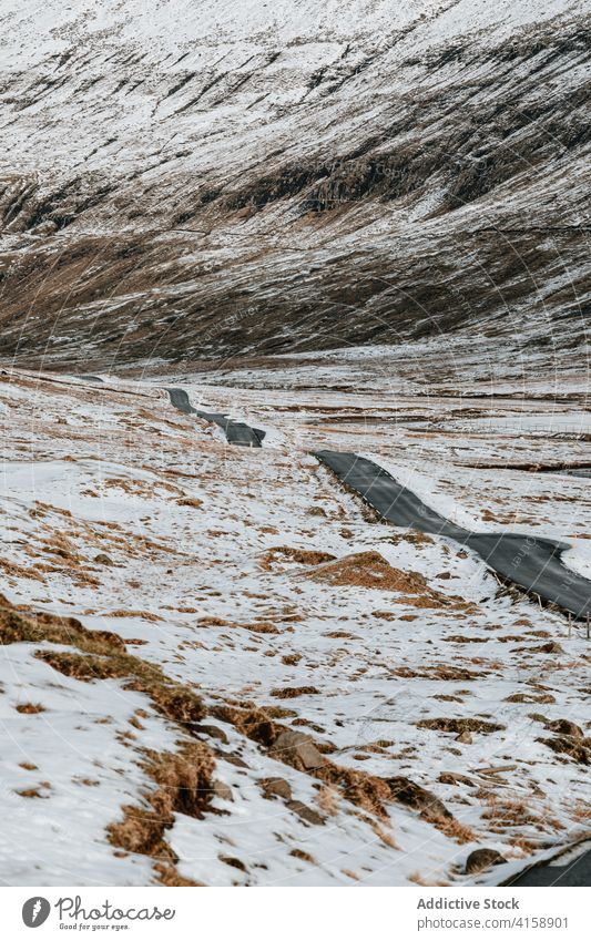 Straße in den Bergen auf den Färöer Inseln Asphalt Berge u. Gebirge Schnee Landschaft leer Natur Winter kalt Fahrbahn wolkig Hügel Ausflug Wetter Saison Weg