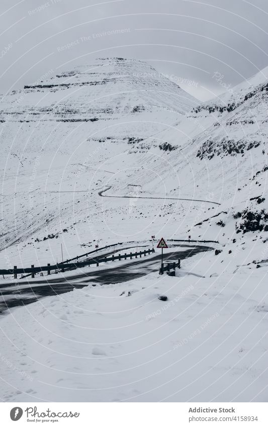 Straße in den Bergen auf den Färöer Inseln Asphalt Berge u. Gebirge Schnee Landschaft leer Natur Winter kalt Fahrbahn wolkig Hügel Ausflug Wetter Saison Weg