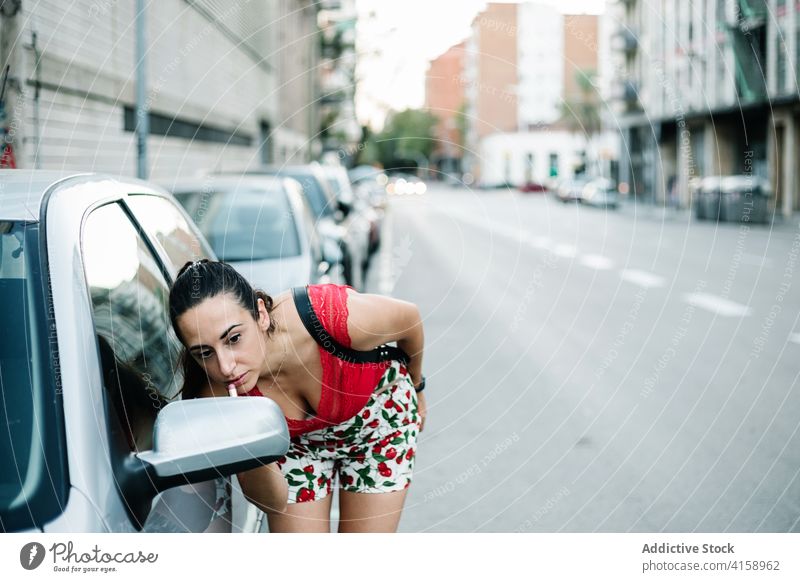 Frau trägt Lippenstift in der Nähe des Autospiegels auf Make-up bewerben PKW Spiegel Straße urban Straßenrand Schönheit Kosmetik jung brünett Glamour Stil Mode