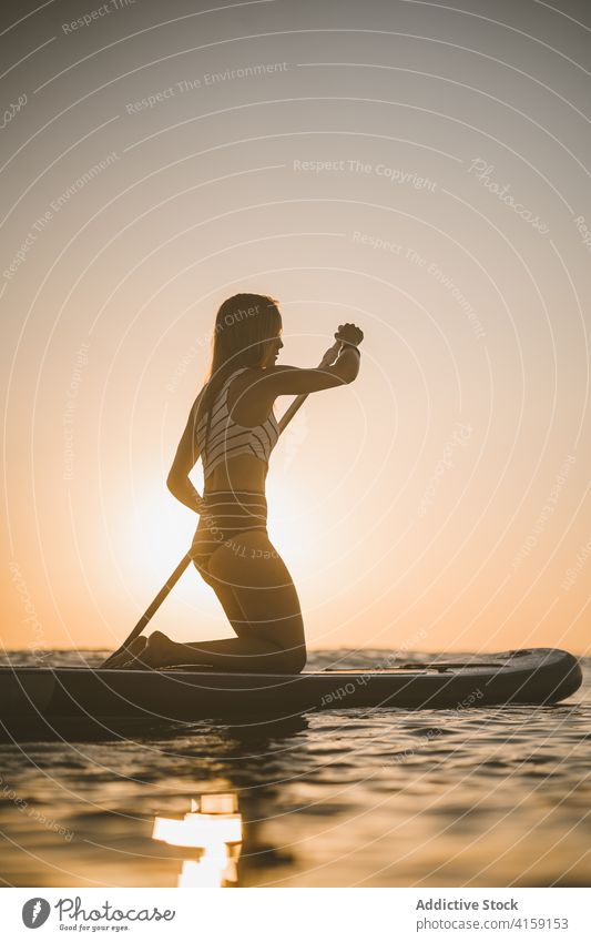 Anonyme Frau rudert auf einem Paddelbrett im Meer Reihe SUP Holzplatte MEER Sonnenuntergang Silhouette Badeanzug Urlaub Sommer sich[Akk] entspannen Wasser