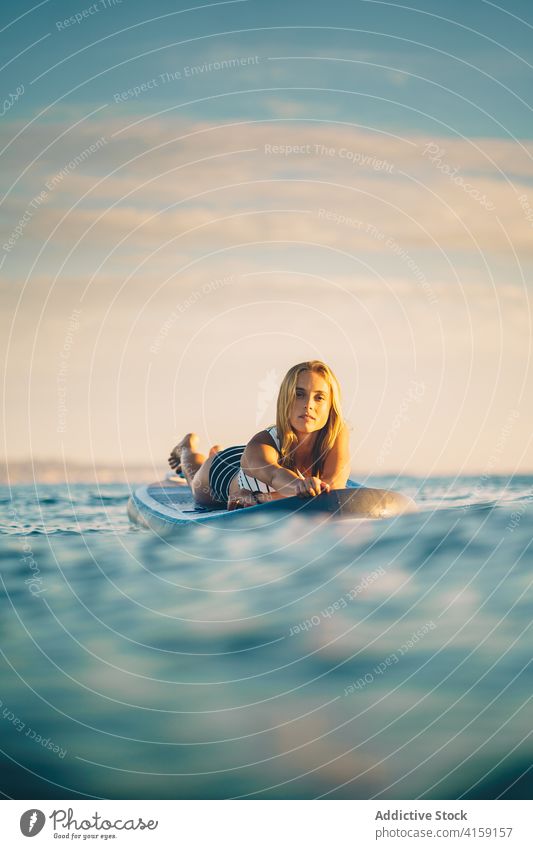 Gelassene Frau auf Surfbrett im Meer Lügen MEER sich[Akk] entspannen Sonnenuntergang schlank Badeanzug Wasser winken Himmel Erholung Sommer Badebekleidung ruhen
