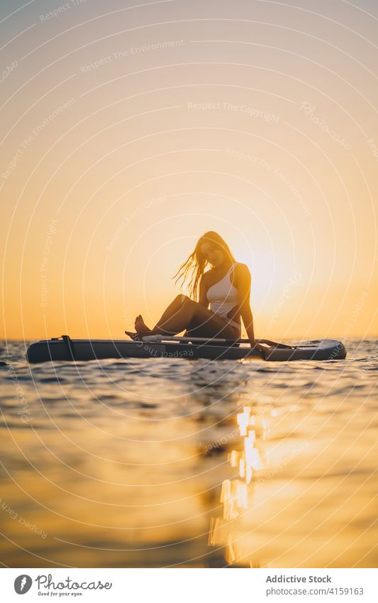 Sorglose Frau auf Paddleboard im Meer Paddelbrett MEER sich[Akk] entspannen Sonnenuntergang SUP Holzplatte Surfbrett schlank Badeanzug Sommer sitzen ruhen