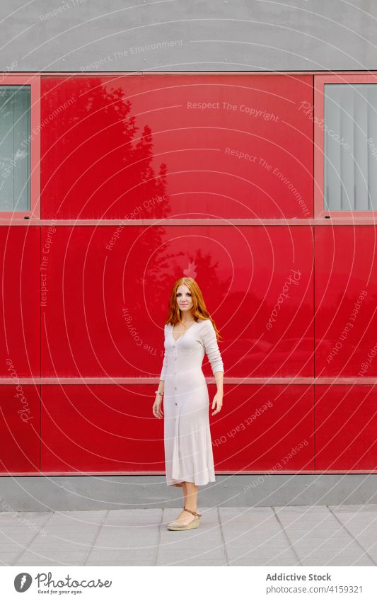 Stilvolle junge Frau steht in der Nähe der roten Wand modern urban Kleid rote Haare trendy Mode Farbe hell Rotschopf Ingwer Zeitgenosse Dame Lifestyle lebhaft