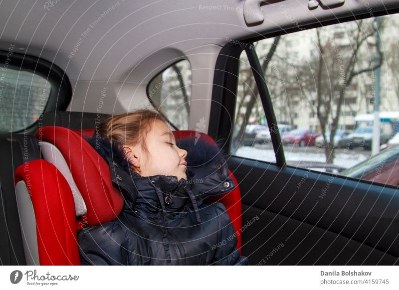 Mädchen in blauer warmer Kleidung sitzt unangeschnallt in einem Autositz und schläft Tochter bequem Rücken Tür rot Fenster sicher Verteidigung sicheres