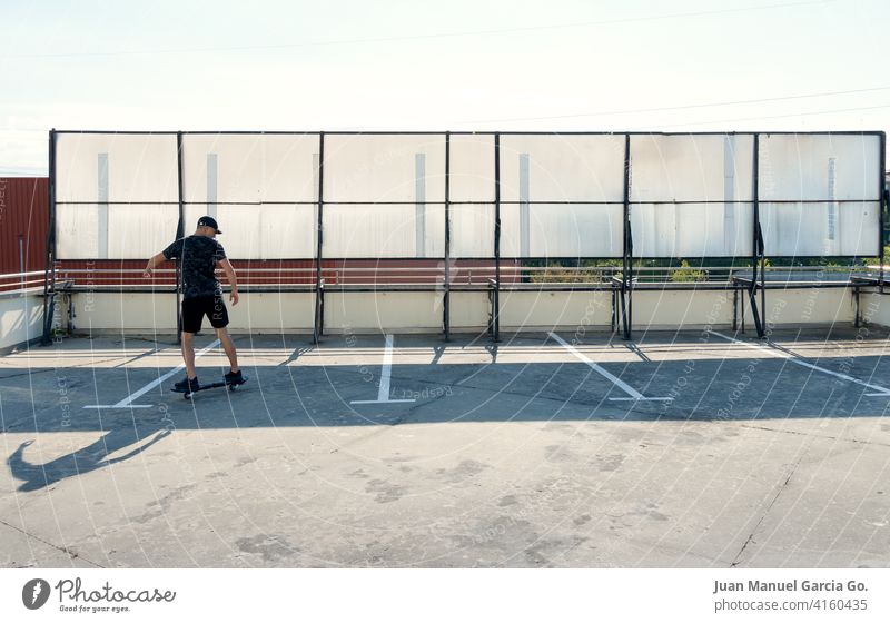 Schwarz gekleideter Teenager mit Mütze beim Skateboarden im Industriegebiet Parkplatz Verlassen abgestufter Haarschnitt solo Dachterrasse Ernsthaftigkeit