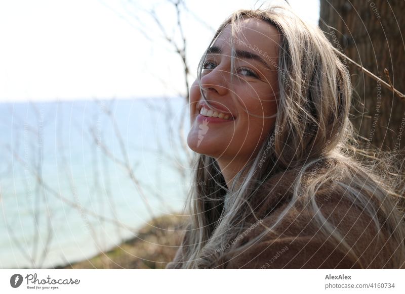 Ein schönes blondes Mädchen steht am Ostseestrand bei der Steilküste, lächelt und schaut in die Kamera Lächeln freudig Landschaft durch Freude Außenaufnahme