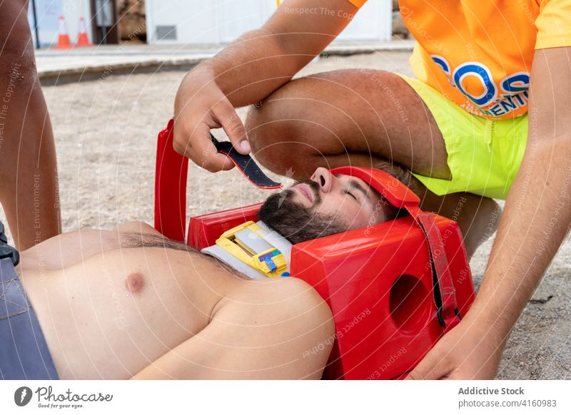 Crop-Rettungsschwimmer rettet Patient mit Halskrause am Strand retten geduldig Unterstützung Training üben Augen geschlossen Klammer Wegfahrsperre medizinisch