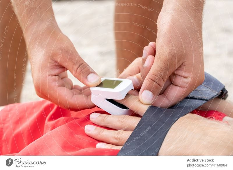 Anonymer Rettungsschwimmer, der den Pulsmesser auf den Finger eines Patienten legt Mitarbeiter geduldig Meter messen Unterstützung Hilfsbereitschaft medizinisch