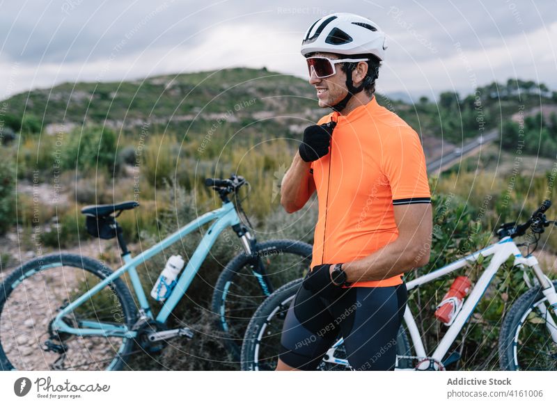 Erfreuter männlicher Radfahrer mit Fahrrad im Hochland Mann vorbereiten Reiter Schutzhelm professionell Gerät Sonnenbrille Sportbekleidung Uniform Aktivität