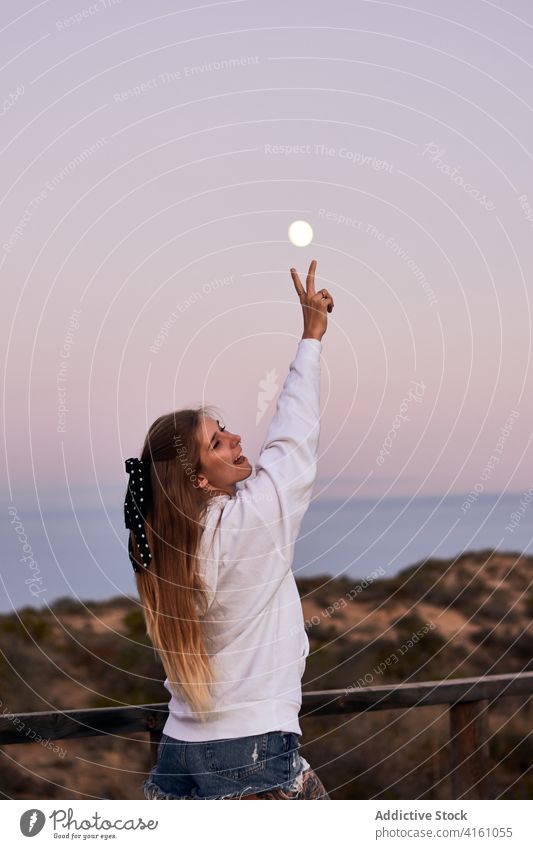 Unbekümmerte Frau zeigt zwei Finger gegen den Himmel bei Sonnenuntergang Frieden Zeichen sorgenfrei v-Zeichen Spazierweg Reisender heiter Glück Urlaub stehen