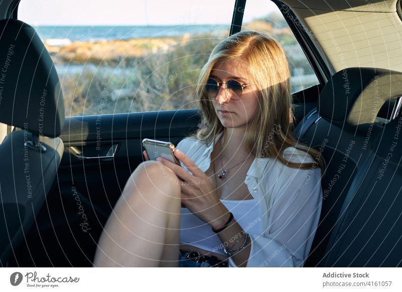 Ruhige Frau mit Smartphone im Auto PKW sich[Akk] entspannen Autoreise Abenteuer Fernweh sorgenfrei Freiheit benutzend Rücksitz Reisender ruhen Feiertag Gerät