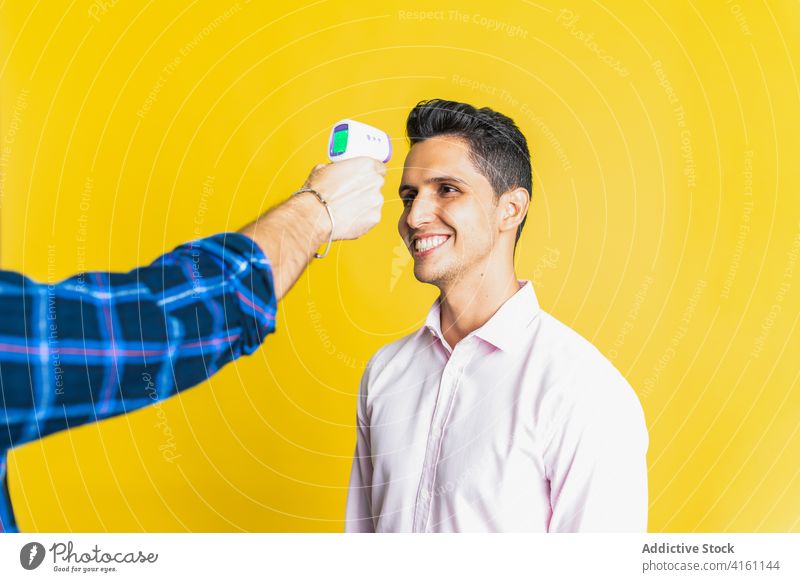 Crop-Mann misst die Temperatur seines fröhlichen Partners mit einem elektronischen Thermometer Männer messen heiter Kollege trendy hell benutzend Gerät modern