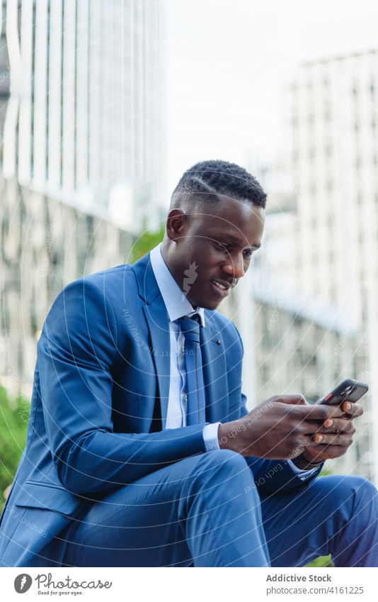 Fröhlicher ethnischer Geschäftsmann benutzt Telefon auf der Straße selbstbewusst reden Glück Erfolg heiter formal urban Anzug modern elegant Exekutive Manager