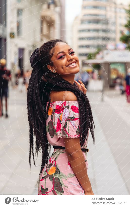 Fröhliche ethnische Frau in modischer Kleidung auf dem Straßenpflaster stylisch Outfit Lächeln freundlich schwarz Afrikanisch Amerikaner Ornament genießen offen