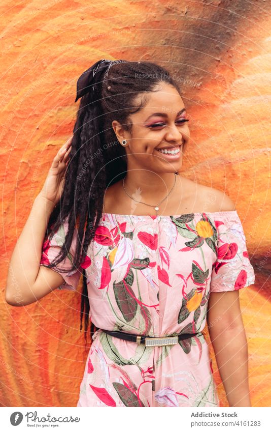 Fröhliche ethnische Frau in modischer Kleidung auf dem Straßenpflaster stylisch Outfit Lächeln freundlich schwarz Afrikanisch Amerikaner Ornament genießen offen