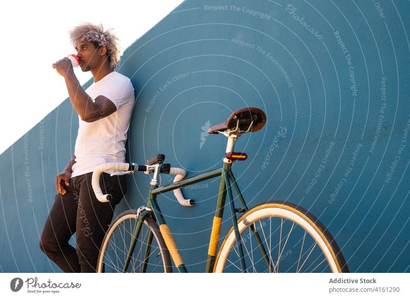 Schwarzer Mann und Afro-Biker trinken Kaffee zum Mitnehmen an einer blauen Wand Schwarzer Biker Schwarzer Reiter Schwarzer Radfahrer Afro-Look Fahrrad