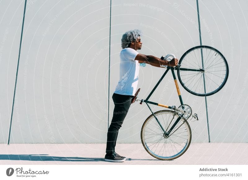 Schwarzer Mann mit Afrofrisur nimmt das Fahrrad und trägt es auf einem grauen Bac Tragen des Fahrrads schwarzer Radfahrer Reiter Schwarzer Reiter Kletterrad
