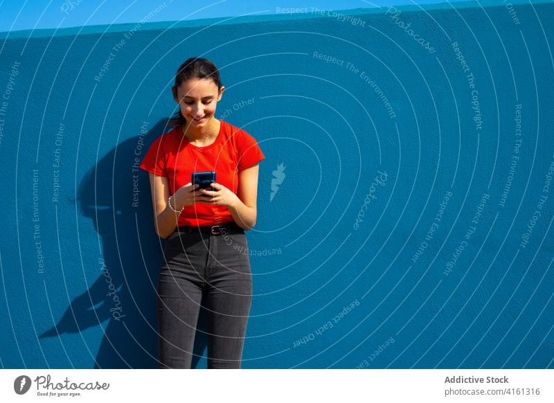 Frau in Rot gekleidet mit dem Handy auf einem blauen Hintergrund. Konzept der Nutzung des Handys. Blauer Hintergrund. Mobile Technik & Technologie