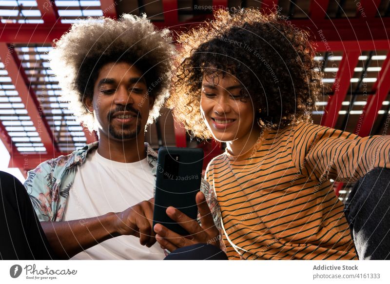 Fröhlicher schwarzer Mann teilt Smartphone mit ethnischem Freund Paar zuschauend teilen Freundschaft Lächeln Internet online Afro-Look benutzend Apparatur Gerät