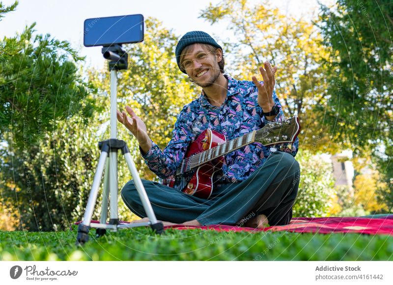 Männlicher Gitarrist nimmt Video im Park auf Aufzeichnen Blogger Mann Gitarrenspieler Musiker Smartphone männlich elektrisch modern Klang Internet