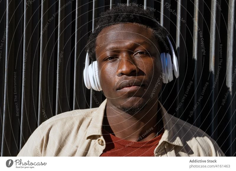 Schwarzer Mann mit Kopfhörern in der Stadt zuhören Musik Straße Windstille Drahtlos Großstadt Gesang melo männlich ethnisch schwarz Afroamerikaner Metall Wand