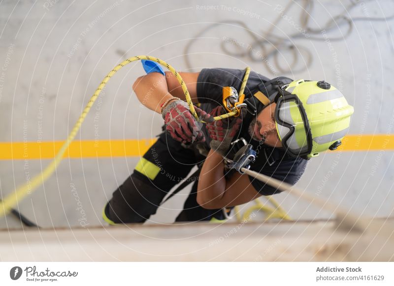 Bärtiger Feuerwehrmann mit Helm klettert bei der Arbeit an einem Seil die Wand hoch Aufstieg Routine üben professionell Sicherheit schützend Fähigkeit Handschuh