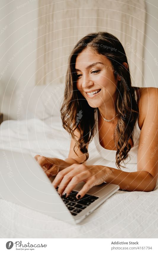 Fröhliche Frau, die auf dem Bett im Laptop surft Morgen benutzend Browsen Glück Schlafzimmer heimwärts heiter jung Gerät Apparatur Internet gemütlich sorgenfrei