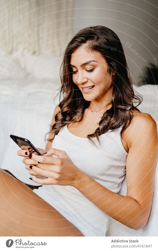 Glückliche Frau mit Smartphone und auf dem Bett liegend charmant sprechen Funktelefon Lächeln Schlafzimmer Inhalt Kommunizieren Apparatur Gerät benutzend