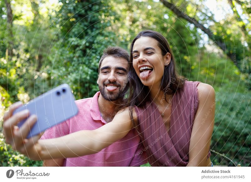 Fröhliches ethnisches Paar nimmt Selfie im Park Zunge Glück Smartphone kuscheln Termin & Datum romantisch Liebe Zusammensein Partnerschaft Apparatur Mobile