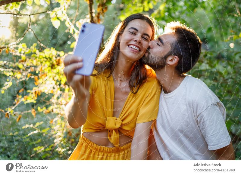 Fröhliches ethnisches Paar nimmt Selfie im Park Kuss Glück Smartphone kuscheln Termin & Datum romantisch Liebe Zusammensein Partnerschaft Apparatur Mobile