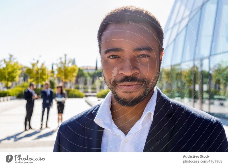 Lächelnder junger schwarzer Geschäftsmann steht auf der Straße in der Nähe eines Glasgebäudes Mann Unternehmer Glück elegant gut gekleidet Gebäude stilvoll
