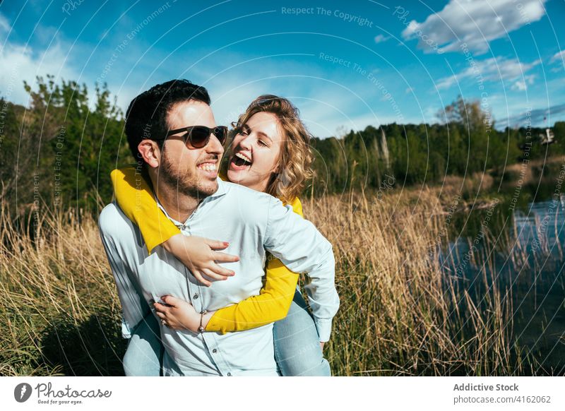 Glückliches Paar hat Spaß zusammen in der Nähe von See Huckepack Spaß haben heiter Umarmung Zusammensein Liebe Freiheit sorgenfrei Freundin Sonnenbrille