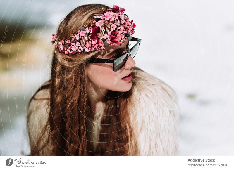 Stilvolle böhmische Frau in Pelzjacke und Sonnenbrille in verschneiten Wäldern sitzend Fell Mode Schnee nordisch Natur Wald Totenkranz Saison Frühling jung