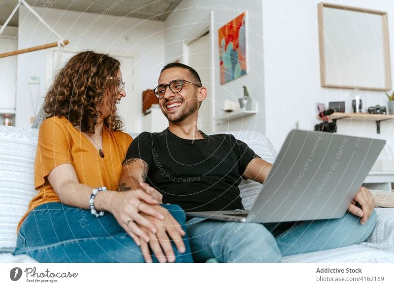 Glückliches Paar mit Video-Gespräch auf Laptop zu Hause Videoanruf Zusammensein Händchenhalten Sofa heimwärts Wellenhand heiter Anschluss Partnerschaft Freund