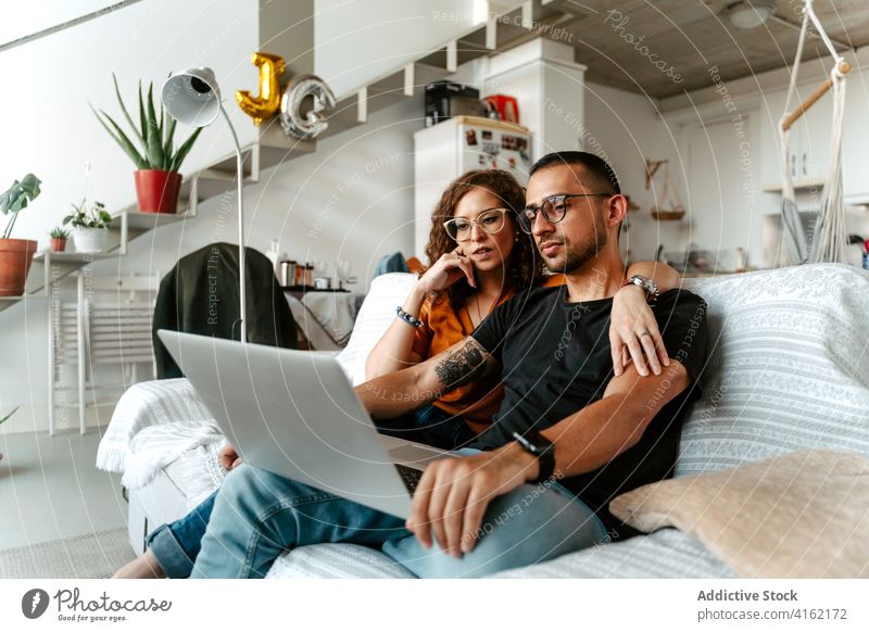 Seriöses junges, vielseitiges Paar, das zu Hause einen Film auf dem Laptop ansieht zuschauen kuscheln sich[Akk] entspannen Sofa Liebe Partnerschaft Zusammensein