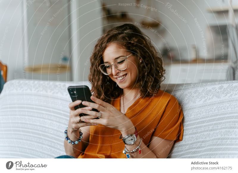 Seriöse Frau, die zu Hause auf ihrem Smartphone surft ruhen Browsen Nachrichtenübermittlung krause Haare Konzentration Raum Kälte Surfen Internet online