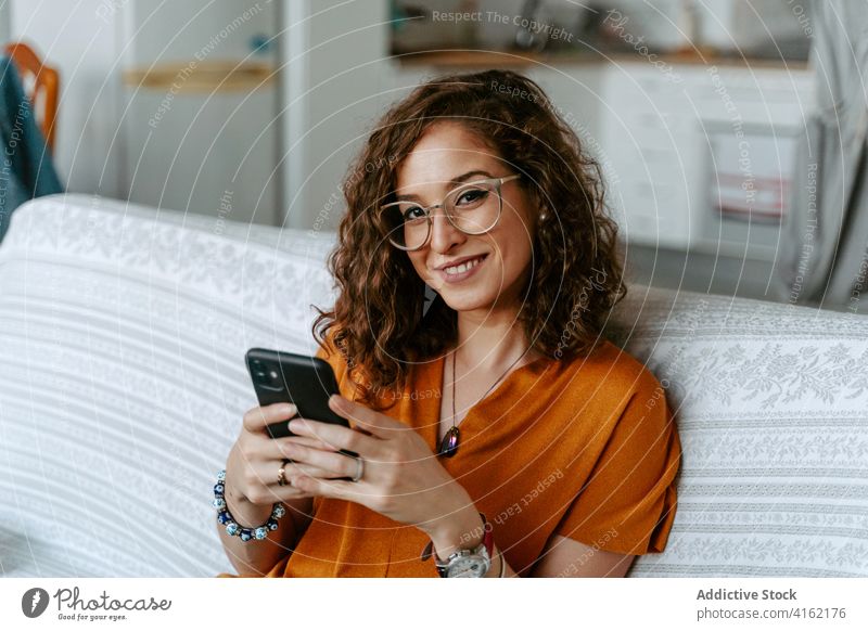 Seriöse Frau, die zu Hause auf ihrem Smartphone surft ruhen Browsen Nachrichtenübermittlung krause Haare Konzentration Raum Kälte Surfen Internet online